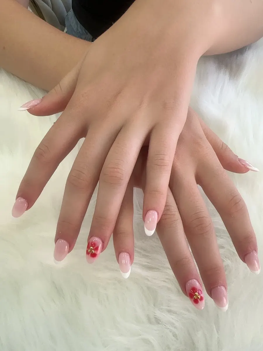Due mani con manicure french rosa e piccola decorazione rossa su un tappeto bianco