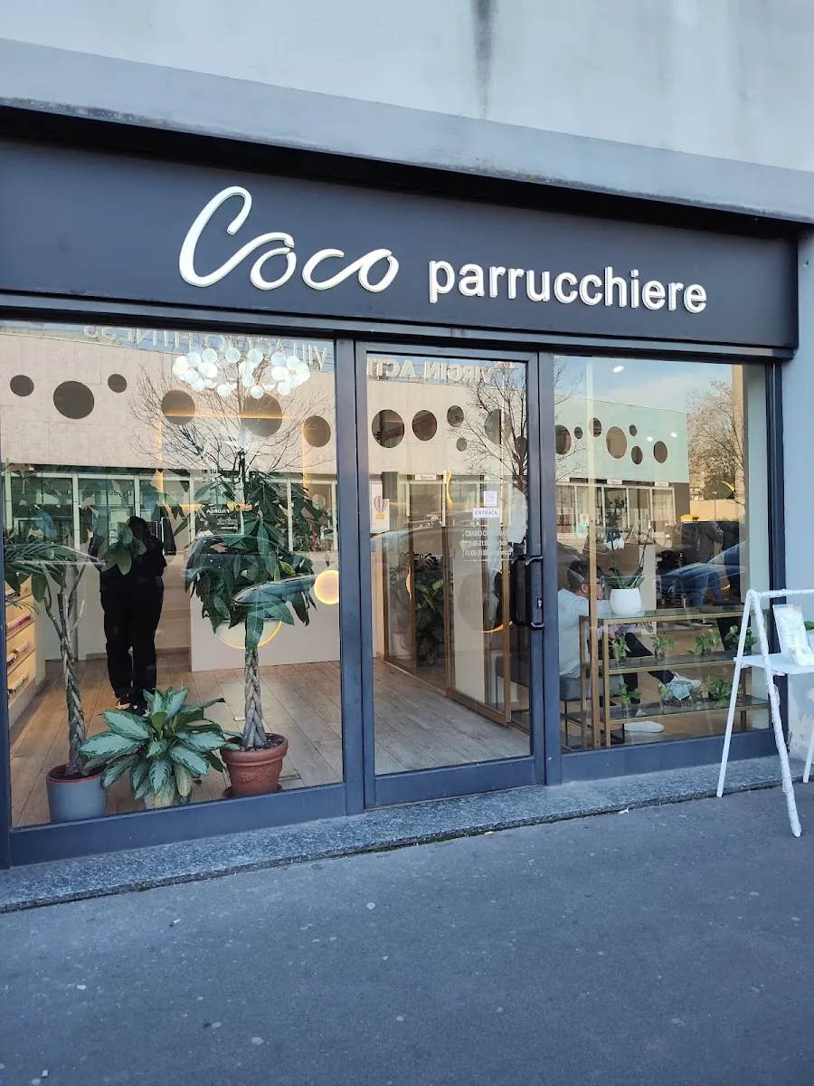 Insegna nera del salone con la scritta corsiva bianca Coco parrucchiere sopra la vetrina