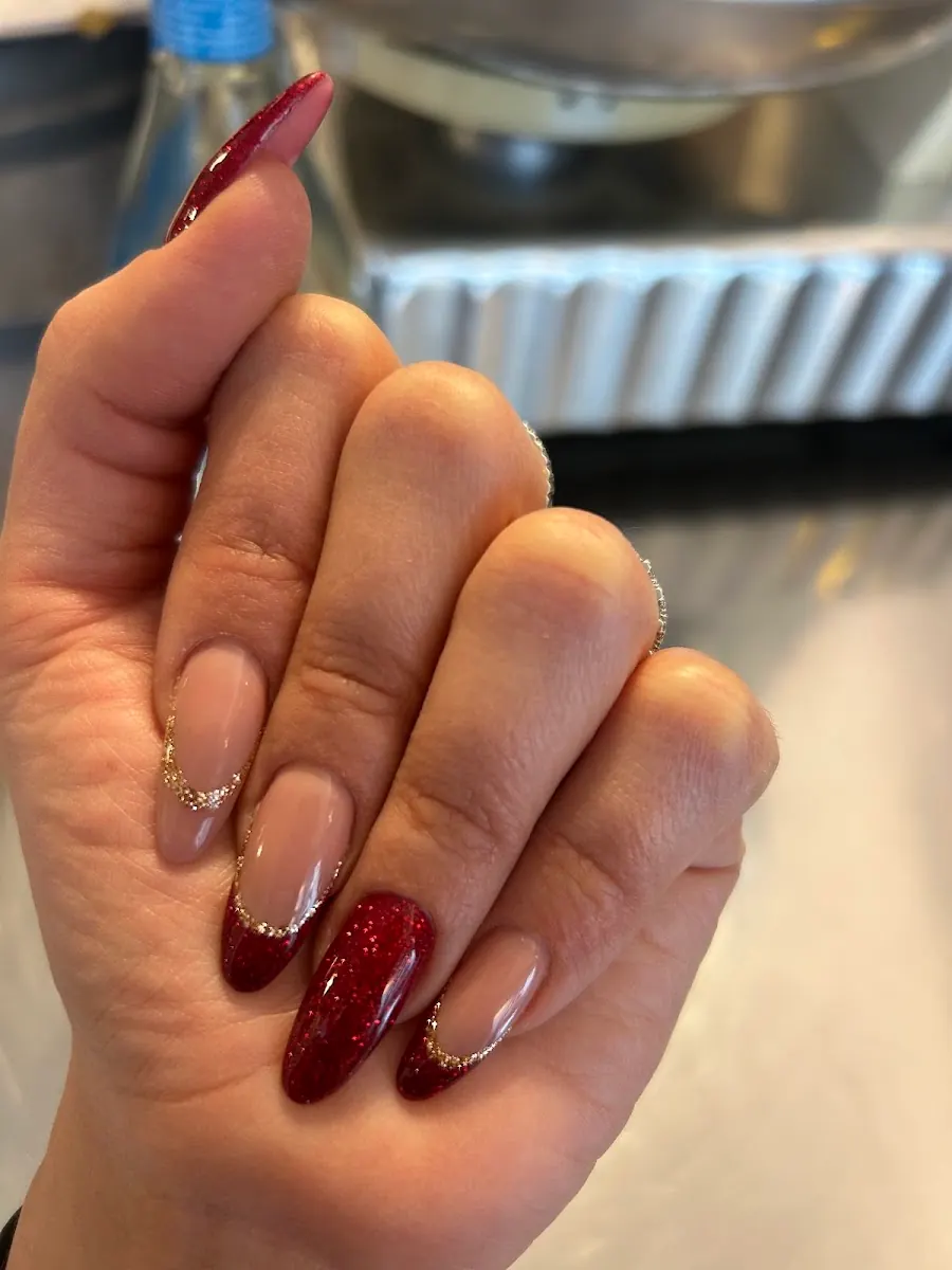Mano con unghie ricostruite a mandorla, smalto rosso e decorazioni dorate