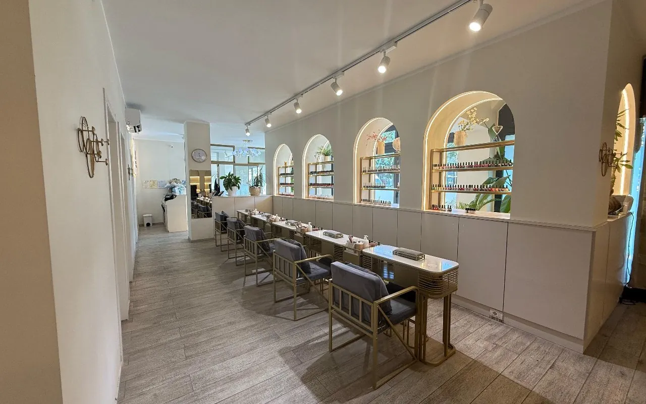 Interno del salone Coco: fila di tavoli manicure in ottone sotto le nicchie ad arco con gli smalti esposti